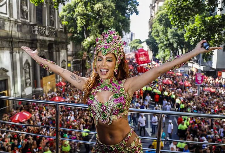 Grande grupo de foliões sorrindo e dançando atrás de um trio elétrico nas ruas do Rio de Janeiro.
