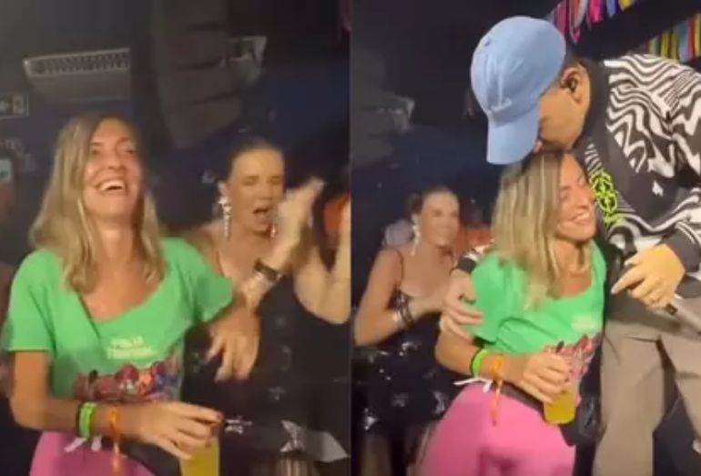 O cantor João Gomes, usando chapéu de vaqueiro, abraça a cientista Tatiana Sampaio no palco de um camarote decorado na Sapucaí.