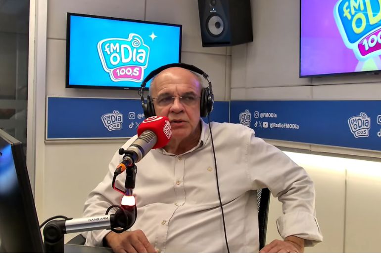 Eduardo Bandeira de Mello em close, gesticulando enquanto concede entrevista em um estúdio.