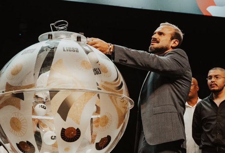 Representantes das escolas de samba e da Liesa no palco da Cidade do Samba durante o sorteio da ordem dos desfiles de 2027, com o logotipo do Rio Carnaval ao fundo.