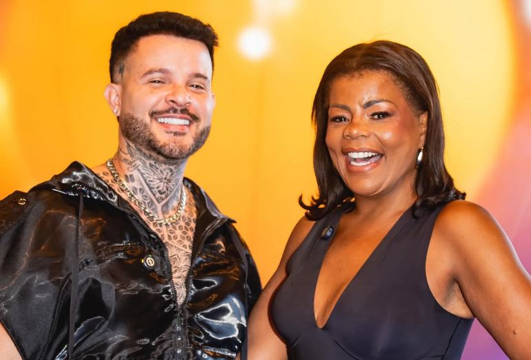 Foto promocional do produtor Hitmaker ao lado da cantora Tati Quebra Barraco, ambos sorridentes em um cenário de estúdio moderno.