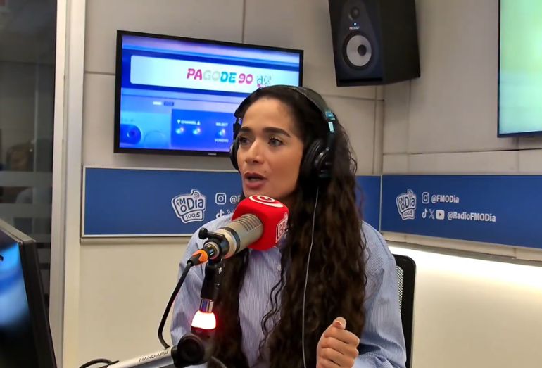 Close da cantora Juliana Fogosa falando com expressividade em um microfone de rádio.