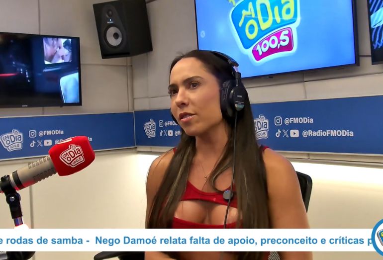 Mulher Melão durante entrevista em estúdio de rádio, gesticulando e sorrindo enquanto fala ao microfone.