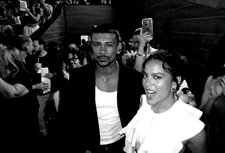 Foto dos atores Xamã e Bella Campos sorridentes durante um evento de divulgação ou tapete vermelho do filme "Cinco Tipos de Medo".