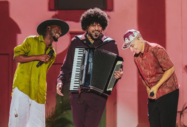 João Gomes, Jota.pê e Mestrinho sorrindo e tocando instrumentos durante show em São Paulo