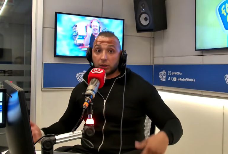 O cantor de funk MC Smith falando ao microfone de forma expressiva e gesticulando durante entrevista nos estúdios da rádio FM O Dia.